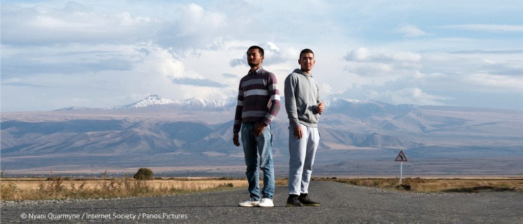 Two men standing on road in Kyrgyzstan in front of a mountain range