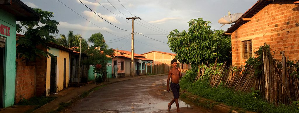 Man walks along unpaved village street in front of house with satellite dish