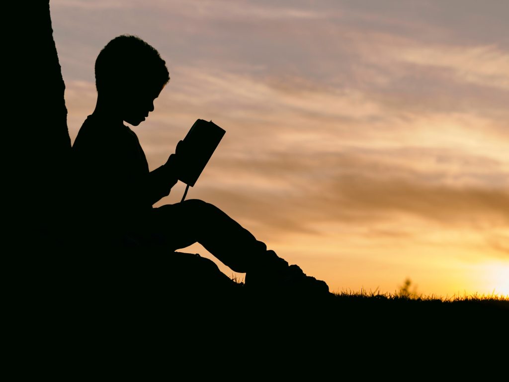 Silhouette of a boy reading in front of a sunset