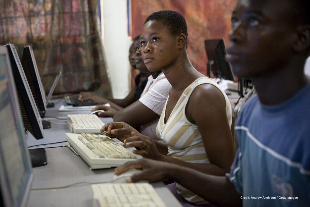 Woman in a classroom working on a computer alongside pupils