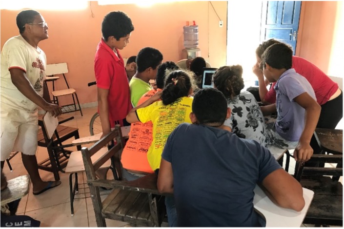 Schoolchildren crowd around a laptop in a classroom