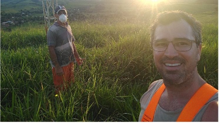 Two Brazilian community network engineers standing in a wide grassy field in front of an antenna