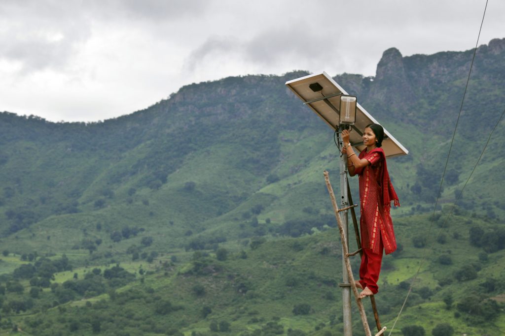 A woman works on a solar panel in front of a mountain hillside