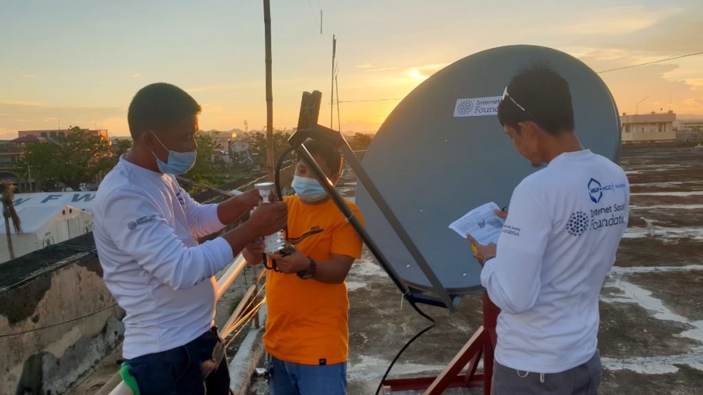 Men wearing Internet Society Foundation and Help NGO shirts assemble a satellite installation on the roof of a building in the Philippines