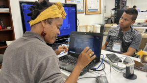 Young woman learning on a laptop with a male instructor watching her work