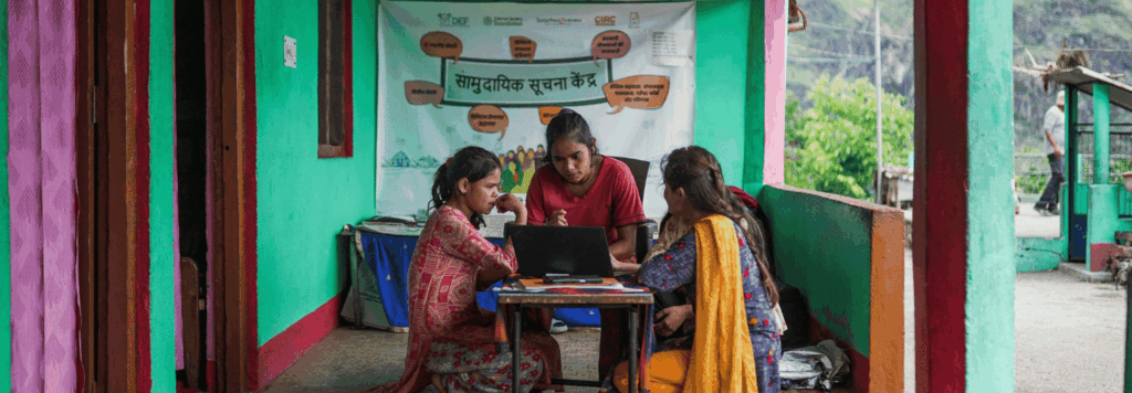 Three women sitting on their legs around a laptop on a small table.