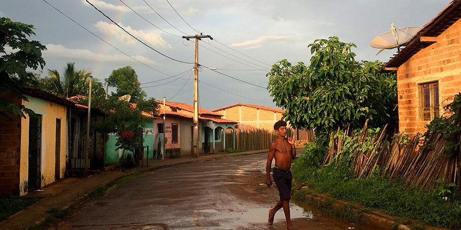 Man walks along unpaved village street in front of house with satellite dish